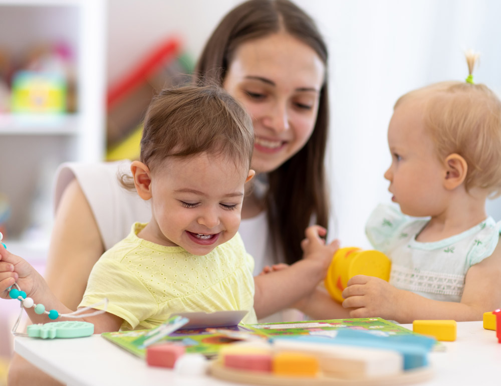 A teacher and two young children engaged in playful activities, with smiles and a colorful learning environment.