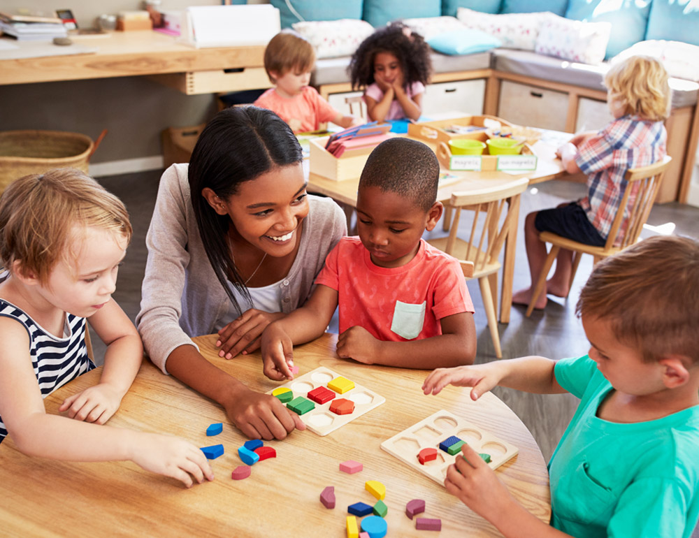 A teacher talking with a group of children at a table, focusing on colorful activities