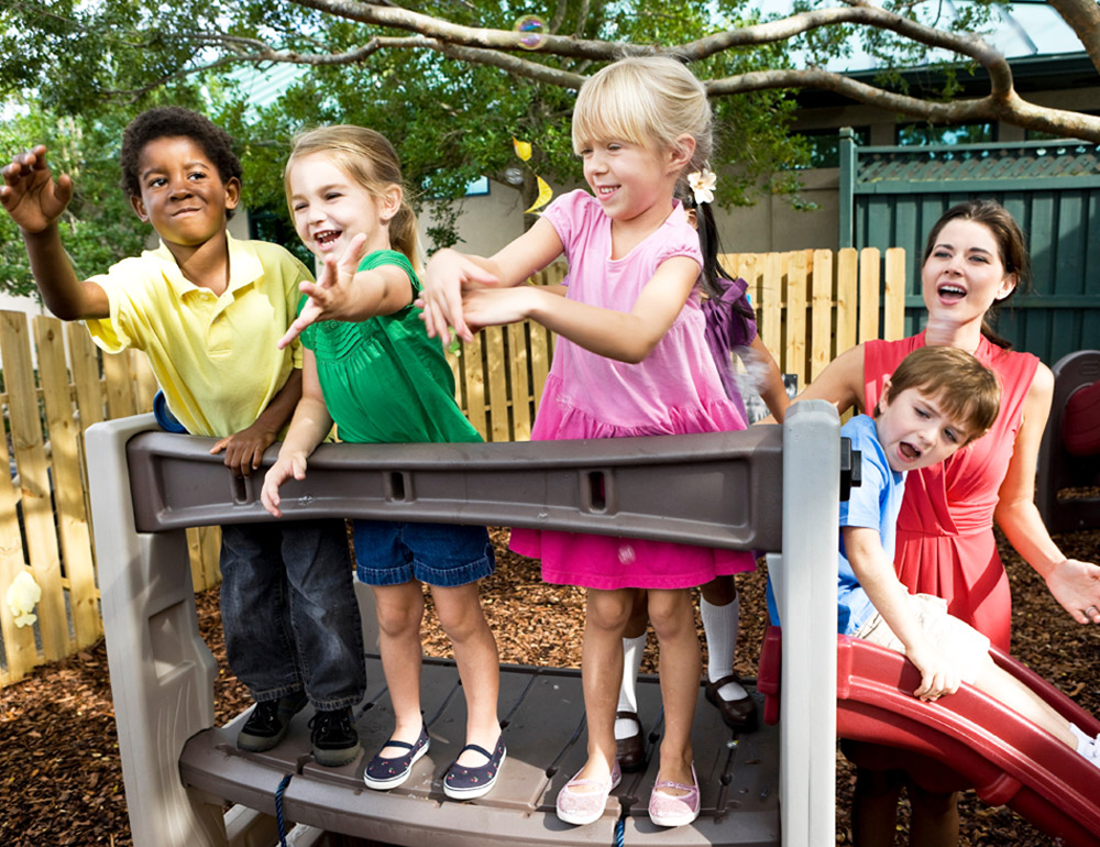 Children playing together on a playground, smiling and enjoying their time with their teacher