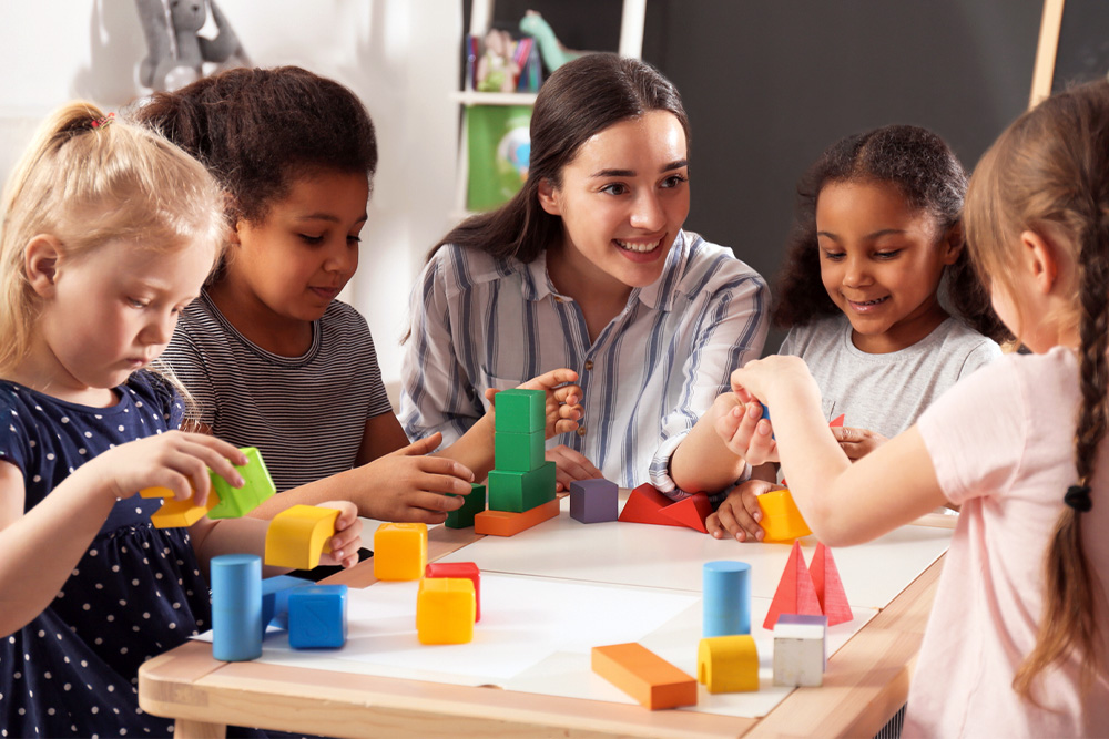 An enthusiastic teacher helping kids with blocks which actively participating and showing excitement.