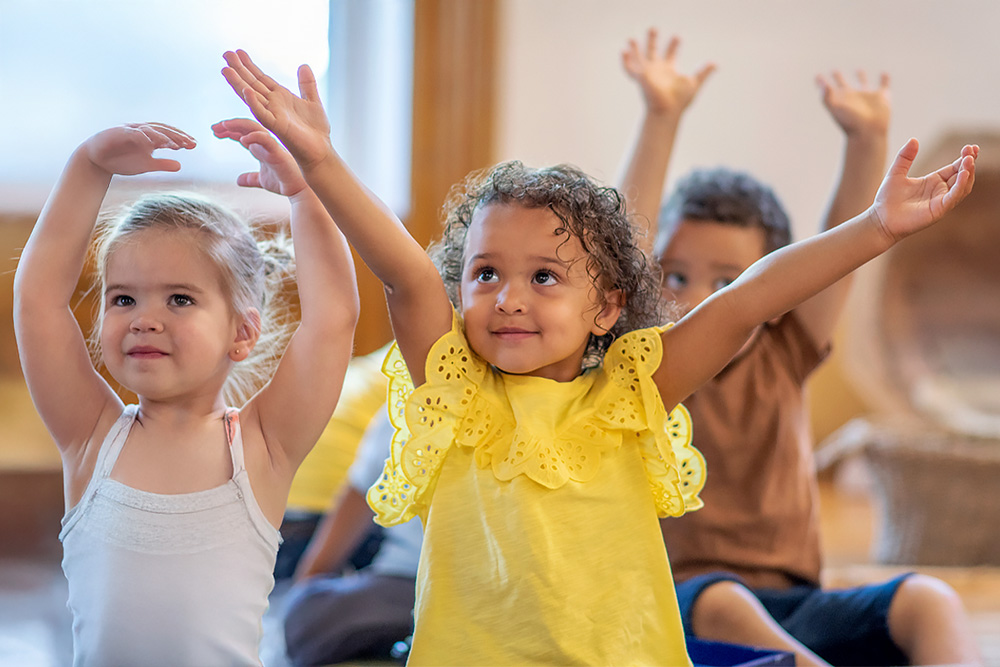 three children smiling and raising their hands, enjoying a playful and engaging environment.