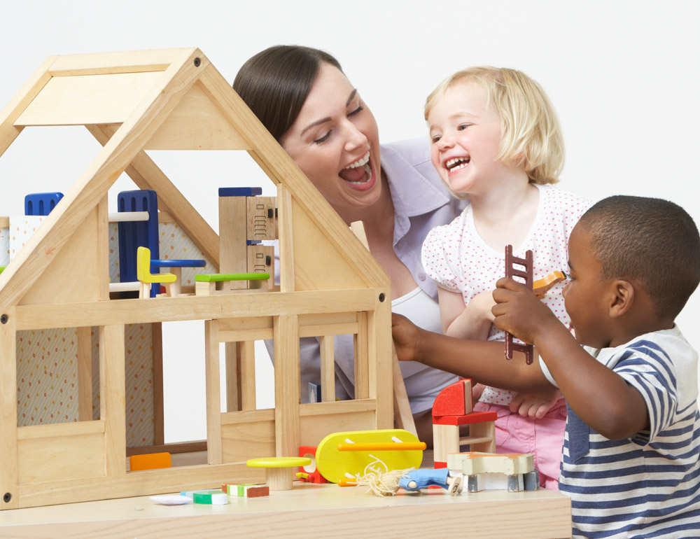 A teacher and two children laughing and playing together with a dollhouse and toys, fun and interactive playtime experience.