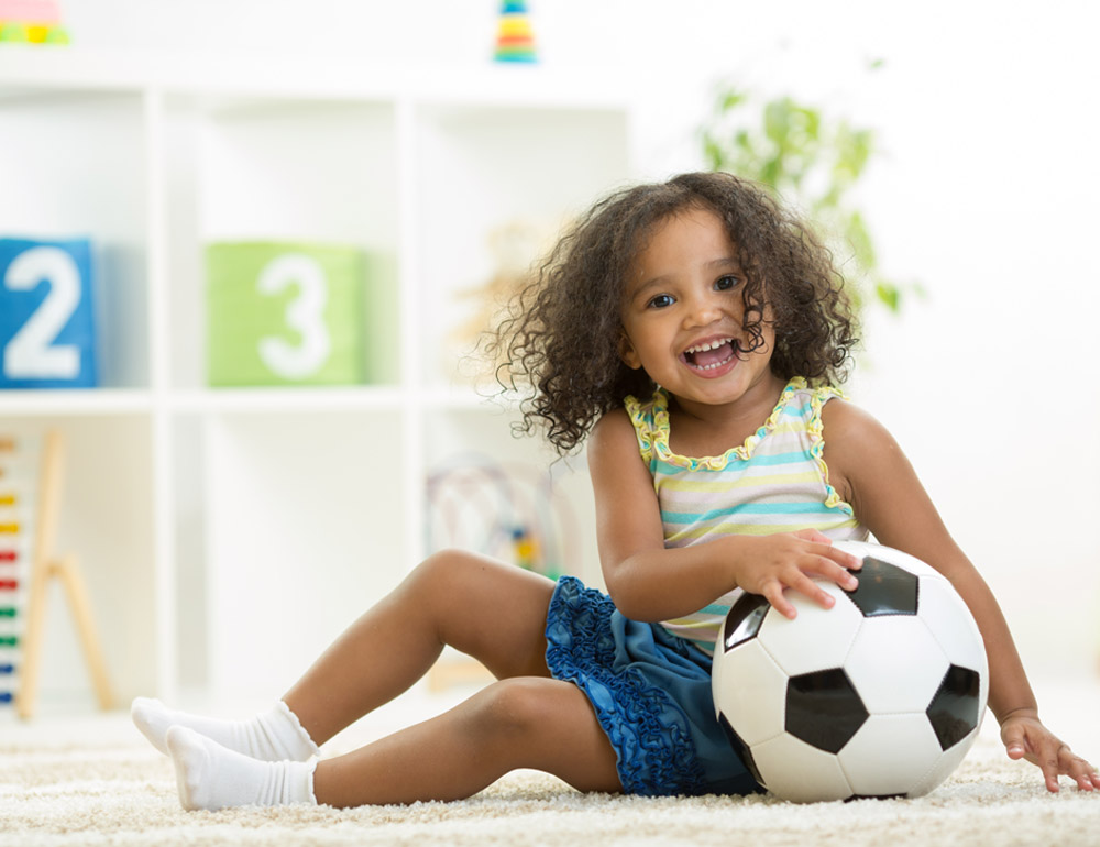 A joyful child sitting with a soccer ball, smiling and having fun.