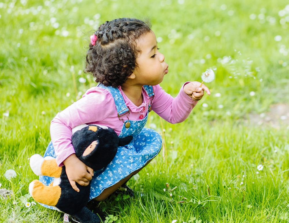 A girl gently blowing dandelion seeds while enjoying a moment in nature.