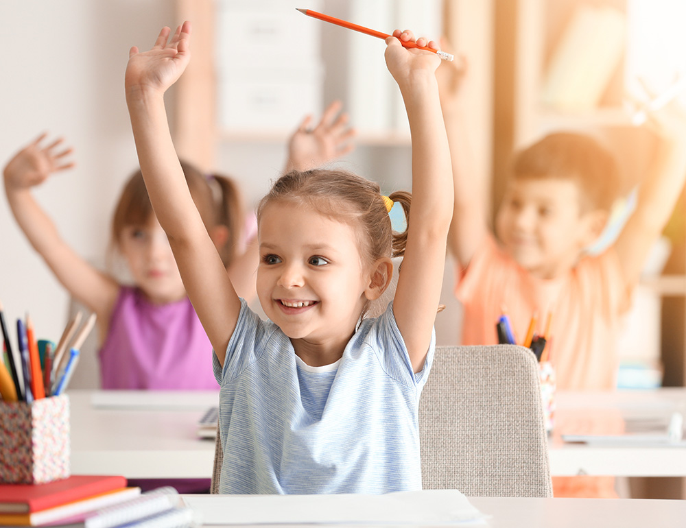 A happy child with raised hands in a classroom, eagerly participating, surrounded by classmates who are engaged as well.