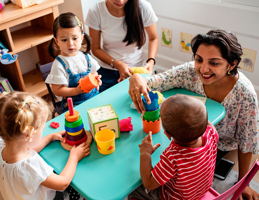 A caring teacher engaging with children as they play with colorful stacking toys, fostering a fun learning environment.