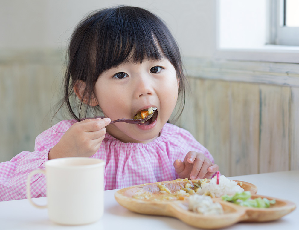 A little girl savoring her food with a joyful expression, sitting at a table with a warm and inviting ambiance.