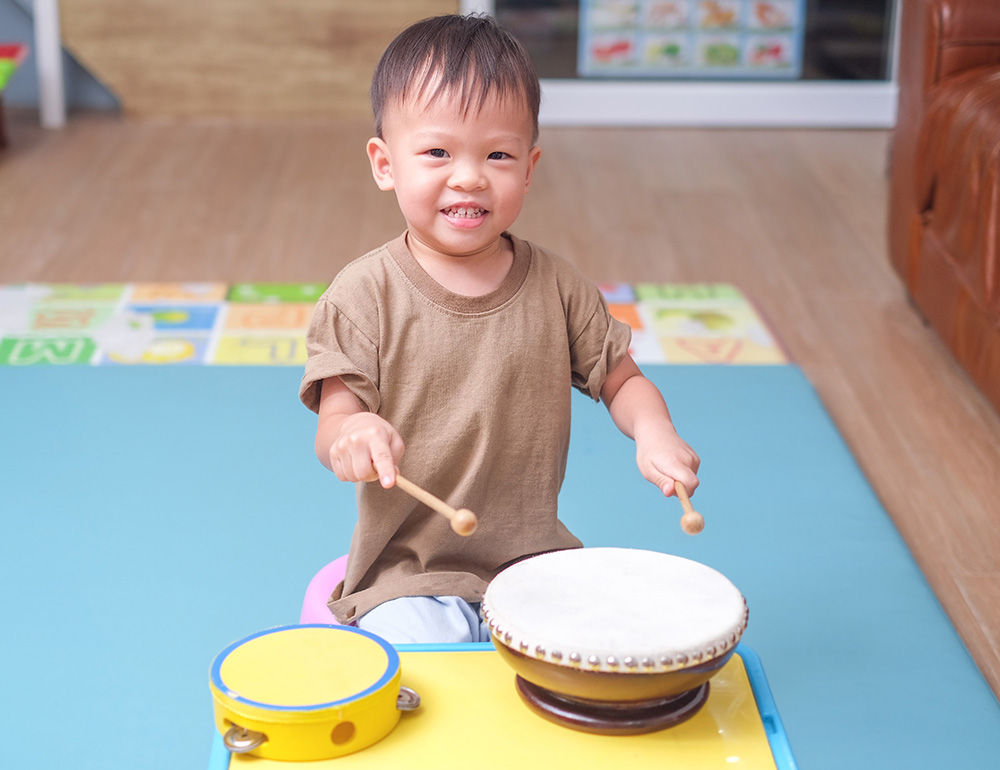 A joyful boy smiling while playing drums with sticks, enjoying his musical playtime.