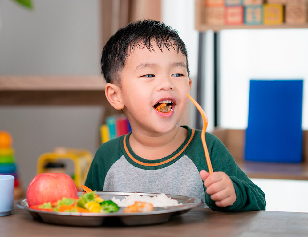 A cheerful little boy enjoying a meal, playfully holding a piece of food, showing a moment of happiness and healthy eating.