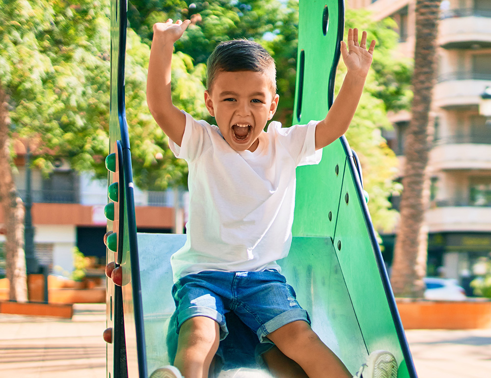 A joyful boy gleefully sliding down a playground slide, embodying pure happiness and excitement in a vibrant outdoor setting.