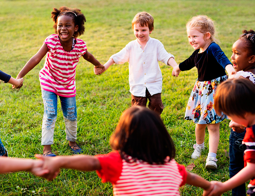 A joyful group of children in a circle, laughing and playing together on a green field, enjoying their time outdoors