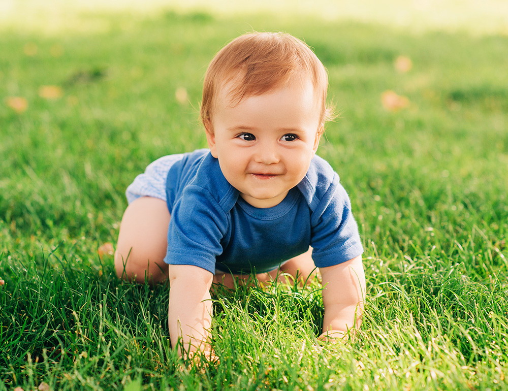 A cheerful baby crawling on lush green grass, enjoying the outdoors and exploring their surroundings with curiosity.