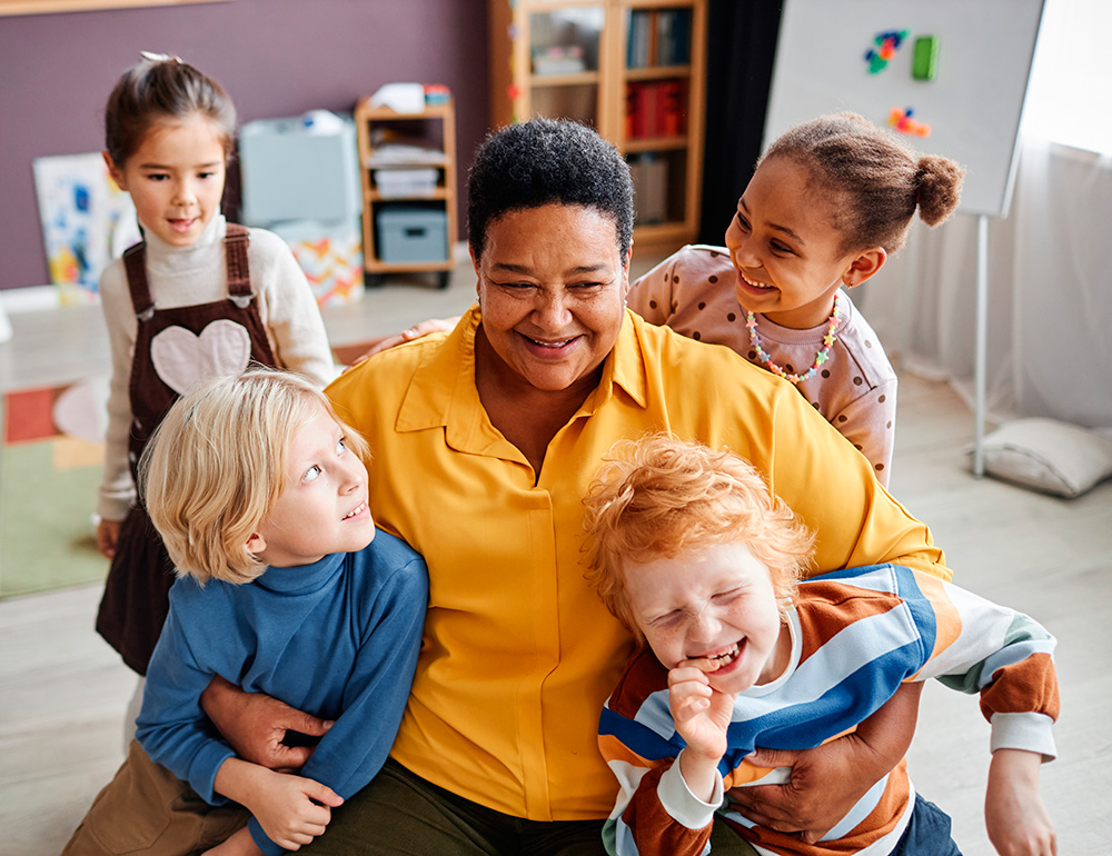 A joyful teacher surrounded by happy children, sharing laughter and connection in a warm, engaging environment.