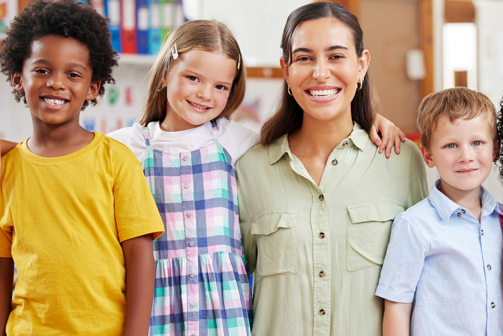 A joyful group of children with their teacher smiling, highlighting faith, love, and learning in a nurturing environment.